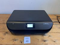 Front view of HP Envy 4516 black all-in-one printer on wooden surface showing power button and LCD screen