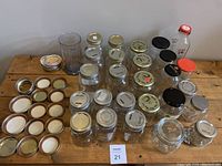 Top-down view of 26 jars including mason jars, lids, and glass containers arranged on a wooden table.