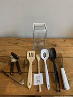 All kitchen utensils and glass container displayed upright on wooden surface against plain background.