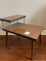 Side view of mid-century modern side table showing two-tier design with wood surfaces and brass rod supports. Scratch visible on upper tier surface.