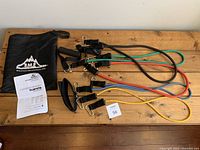 Photo showing entire set including multiple resistance bands in black, green, red, blue, and yellow colors, black carry bag branded with Black Mountain Products logo, instruction manual, and some accessories.