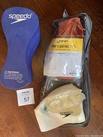 Photo showing a purple Speedo buoy training aid, white Speedo swimming cap, and clear swim goggles on a wooden floor.