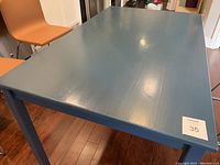 Blue painted rectangular wooden table with visible wood grain, surface wear and scuffs visible under bright lighting.