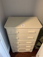 Front angle view of cream tallboy dresser showing drawer handles and some wear.