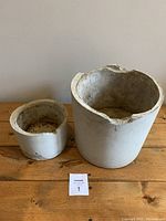 Two cement planters, large and small, placed on wooden surface against wall with item card visible.