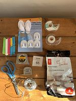 Photo showing complete contents of utility drawer lot including scissors, tape measures, tape rolls, packet clamps, utility hooks, and tea light candles on wooden background.