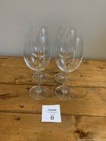 Four clear stemmed wine glasses with large rounded bowls displayed on wooden surface.