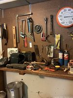 Full view of workbench with assorted hand tools including clamps, pliers, and a Taylor wall thermometer on pegboard.