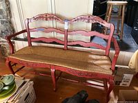 Full front view of vintage red wooden bench with carved details and wicker seat, showing overall shape and condition.