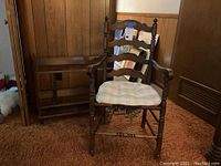 Full view of chair with cushion and wood bookshelf side by side on carpet floor in wood-paneled room.