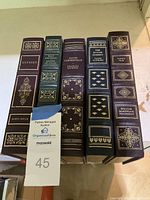 Five classic books from the Franklin Library lined up side by side, showing gold embossed details on spine covers including Ulysses, Leaves of Grass, David Copperfield, The Divine Comedy, and Vanity Fair.