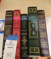 Spine view of five hardcover classic books including The Portrait of a Lady, Pride and Prejudice, The Adventures of Huckleberry Finn, Tom Jones, and Selected Stories. All have decorative gold embossing on spine.