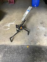 Clay pigeon thrower positioned inside a garage, showing the full device including tripod legs and launch arm.