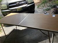 Full view of one folding table with metal frame and brown woodgrain formica top, showing overall condition.