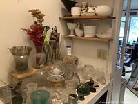 Kitchen counter with multiple glass vases including clear, aqua, and green colors, ceramic and glass containers, domes, and small decorative pieces