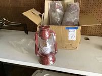 Six kerosene oil lamps, one displayed outside of box, others in bubble wrap inside cardboard boxes on table