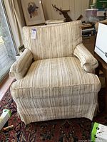 Front view of vintage upholstered cream chair with brown stripes and fabric arm covers.