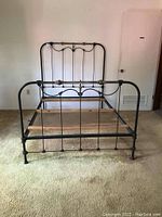Full view of the vintage metal bed frame showing headboard with vertical bars and brass ornaments.