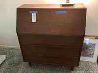 Front view of vintage wooden secretary desk showing drop-front front panel and three drawers below.