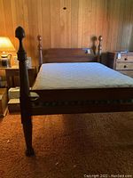 Full view of wooden bed frame with mattress in bedroom, showing front posts and headboard.
