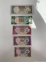 Front sides of five Kuwaiti banknotes in uncirculated mint condition, showing Arabic text and emblem.