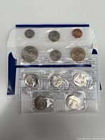 Plastic sealed proof coins from USA 2005 proof set showing multiple coins including penny, nickel, dime, quarters, seals, and information inserts.