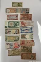 Photo of 13 various world banknotes, assorted denominations and designs from different countries laid out on a white surface