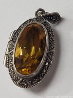 Close-up front angled view of oval locket pendant with faceted citrine stone surrounded by marcasite accents in sterling silver.