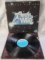 April Wine Forever For Now vinyl record partly removed from sleeve showing blue label and black vinyl surface, in very good condition.