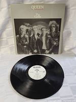 Photo of Queen The Game vinyl LP with cover behind it, showing black vinyl and white label.