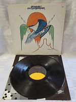 Front side of LP vinyl and album cover upright behind it. Shows the vinyl's black surface and center label and cover artwork.