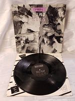 Black and white artistic collage cover of The Spoons 'Telling Lies' LP with the vinyl record partially removed showing black label with album title and band.