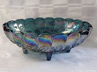Side angled view of the blue carnival glass fruit bowl with scalloped edge and three legs showing iridescent surface.