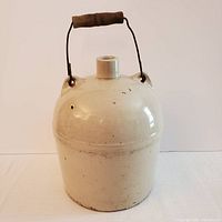 Full side view of antique ceramic bottle with metal wire handle and wooden grip, showing overall shape and color.