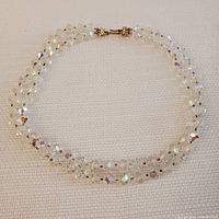 Full view of the double-strand Aurora Borealis glass bead necklace laid flat on a textured beige surface to show its length and bead arrangement.