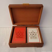 Wooden box open showing two decks of playing cards inside; orange deck and white deck both feature Canadian Centennial stylized maple leaf design dated 1867-1967.