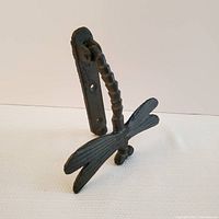 Side angle view showing the dragonfly-shaped door knocker with textured wings and segmented body mounted on a plate with screw holes.