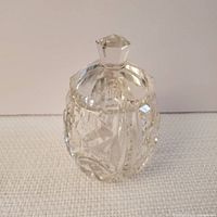 Clear crystal salt cellar with lid, showing diamond and cross cut patterns on the side and faceted finial on lid.
