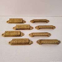 Front view of eight ornate solid brass drawer pulls showing detailed decorative patterns.
