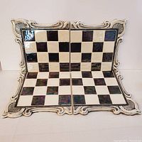 Four ceramic chess board tiles arranged to show their iridescent black and white squares and decorative borders, assembled to display the full chessboard pattern.
