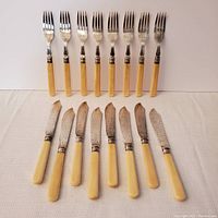 Full set of eight fish forks and eight fish knives laid out on cloth background