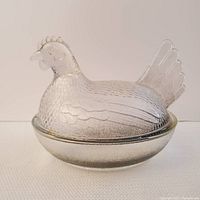 Front view of the vintage clear pressed glass hen dish sitting on its basket base, showing detailed feather texture and comb on the lid.