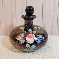 Front view of the iridescent glass bottle showing the painted floral pink rose design and stopper on top.
