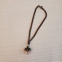 Full view of silver chain bracelet with heart charm pendant on white textured fabric.