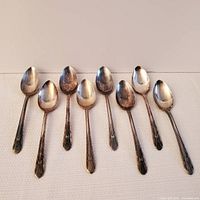 Eight silver plate spoons laid on a light textured surface showing overall set appearance