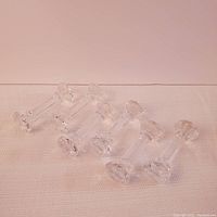 Six crystal utensil rests arranged in a row on a white cloth surface, showing their overall shape and condition.