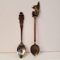 Pair of souvenir spoons showing front sides, one with Canada crest handle, other shaped like Quebec with ruler handle.