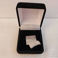 Front view of the sterling silver CIBC 1B award pin in the black velvet box with white satin lining.