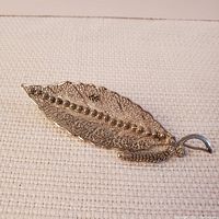 Filigree silver leaf brooch showing full piece with twisted wire detail and beaded central vein, placed on a neutral fabric.