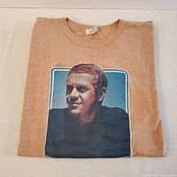 Folded tan cotton T-shirt showing full front photographic image of Steve McQueen.